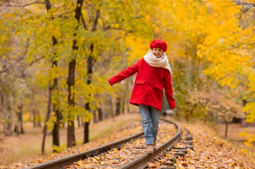 Caucasian girl in a red coat and beret walks along the railway tracks in the park in autumn