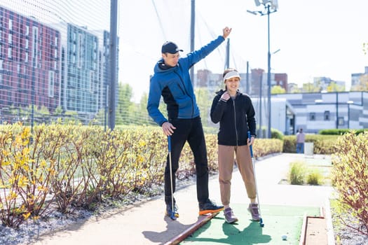 The girl is preparing to hit the ball with a golf club and looks at the man who is squatting next to her with the golf club in his hands. High quality photo