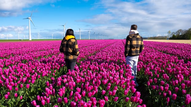a couple of men and women standing gracefully in a vibrant field of purple tulips, surrounded by the beauty of a Dutch spring. A diverse couple in a tulip field in the Netherlands