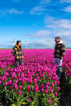 Two men standing tall in a sea of vibrant purple tulips, surrounded by windmill turbines in the Dutch countryside during Springtime.