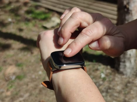 finger of a woman's hand on the screen of a smart watch in sunlight close-up