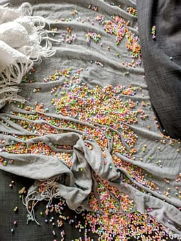 Colourful small tiny beads are laying in a mess on a sofa covered with blankets. High quality photo. Kids messy play, kids' game. Mess after kids