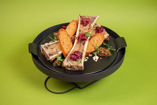 Roasted bone marrow with toast, herbs on black plate, isolated on green. Modern restaurant dish concept. Selective focus, close-up