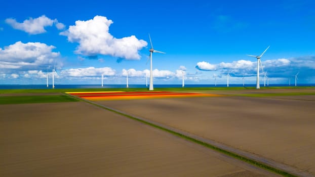 A serene landscape unfolds before us, with a vast field stretching out beneath a clear spring sky. In the background, a collection of windmills stands tall and proud, harnessing the power of the wind.