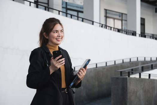 A woman in a business suit holding a cell phone and a briefcase. She is smiling and she is happy