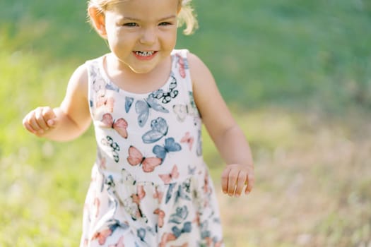 Little laughing girl walks on a green lawn. High quality photo
