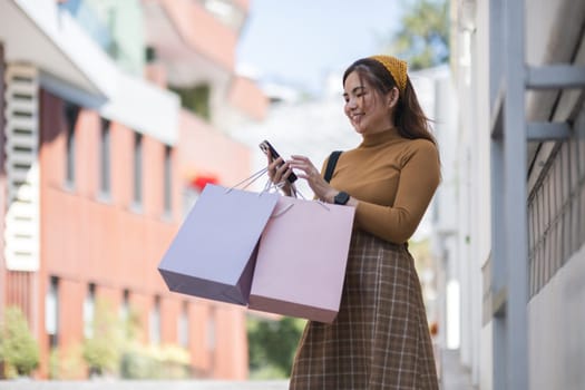A woman is holding two pink shopping bags and looking at her cell phone. She is smiling and she is happy