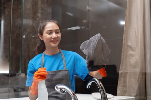 Asian woman cleaning the glass in the apartment. Cleaning staff maintain cleanliness in with towel and spray detergent.