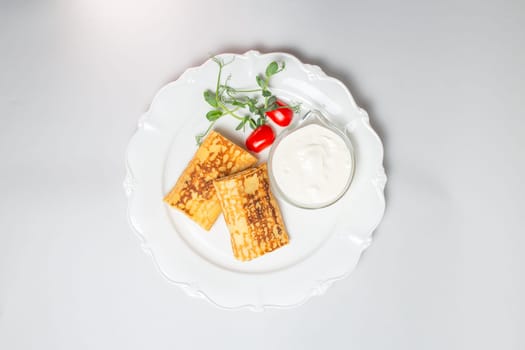 Top view of Pancakes with sour cream and cherry tomatoes on a white background. Carnival menu.