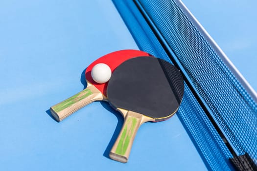 Two table tennis or ping pong rackets and ball on blue table with net. High quality photo