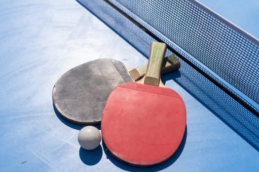 Red and black Table Tennis Paddles and ball on the blue table tennis table with net. Ping Pong concept with copy space. High quality photo