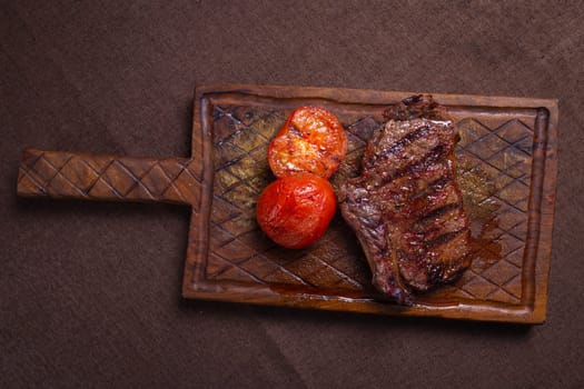 A succulent beef steak, perfectly grilled, served with tomatoes on a wooden board. Ideal for a delicious lunch or dinner.