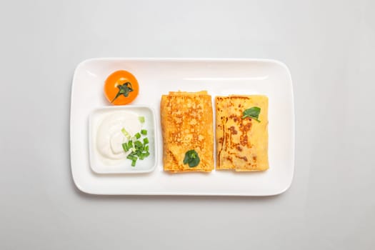 Two folded stuffed savory crepes with sour cream and chives garnish on a white plate on a white background.