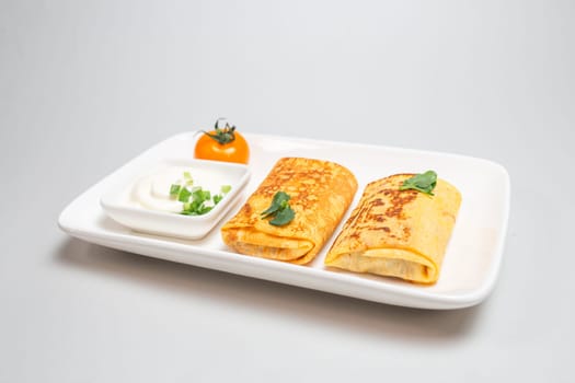 Two folded stuffed savory crepes with sour cream and chives garnish on a white plate on a white background.