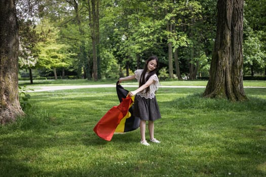 Portrait of one beautiful Caucasian little brunette girl in a skirt with flowing hair twirling with a Belgian flag in a city park on a summer day, close-up side view.