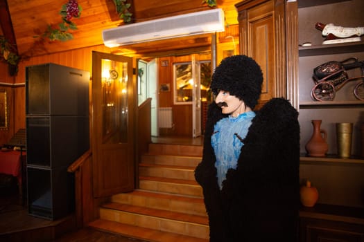 A man with a beard and mustache is wearing a fur coat and hat. He is standing in a restaurant with a rustic interior.