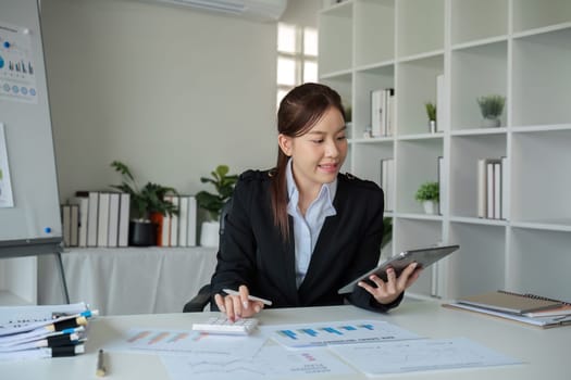 Young woman accountant uses calculator to calculate finances or graph business numbers on white wooden table in office..