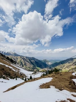 Blue sky with clouds, snowy ground, mountains, valley, ski resort in distance. Scenic winter landscape view.