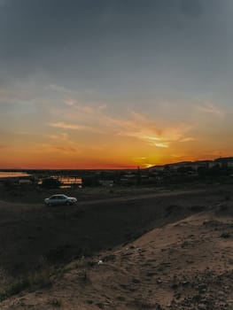 A car parked on a hill, sunset colors the sky, city lights twinkle. Scenic view, travel vibes, wanderlust adventure.