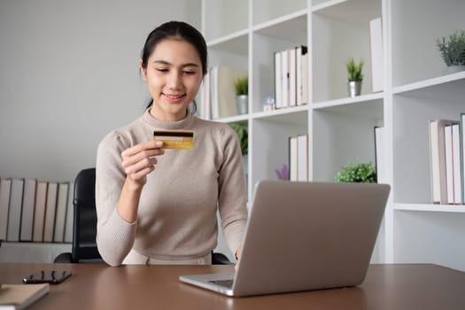 Beautiful young woman uses laptop to shop online, buys things and pays with credit card through phone online banking app..