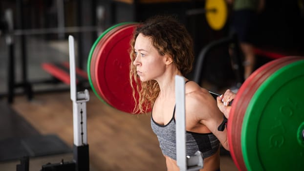 Middle-aged woman doing squats with a barbell in the gym