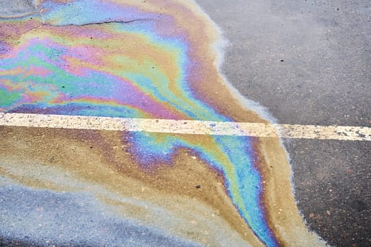 Oil spillage on wet pavement, parking lot with dividing lines, underscoring the environmental obstacles tied to water pollution.