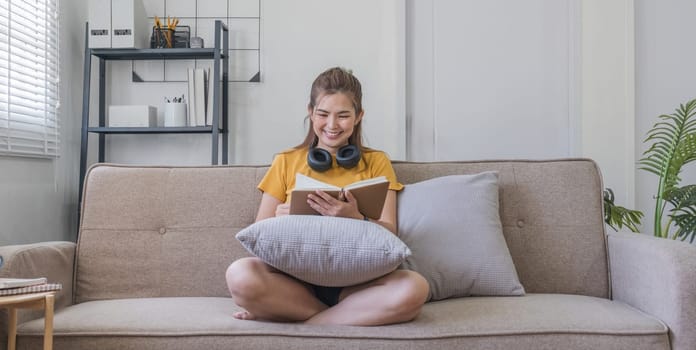 A woman sits on a sofa reading a novel on her lap..