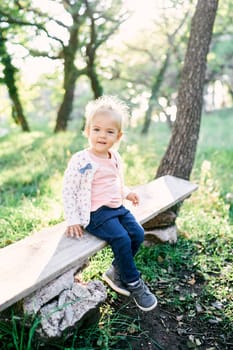 Little smiling girl sitting on a bench in the forest. High quality photo