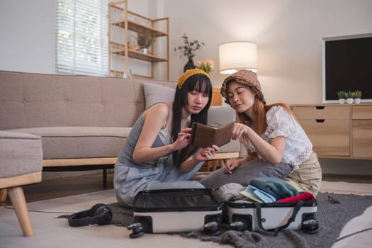 Two women sitting on the floor with suitcases Both of them were checking their passports. They are planning to go on vacation..