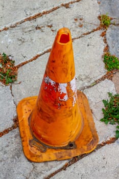 This battered orange traffic cone stands as a weathered symbol of the wear and tear endured on the roads, serving as a reminder of safety measures and road maintenance