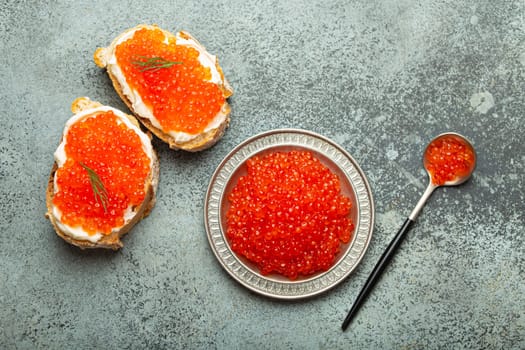 Small metal plate with red salmon caviar and two caviar toasts canape top view on grey concrete background, festive luxury delicacy and appetizer.