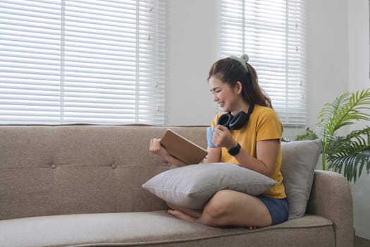 A woman sits on a sofa reading a novel on her lap..