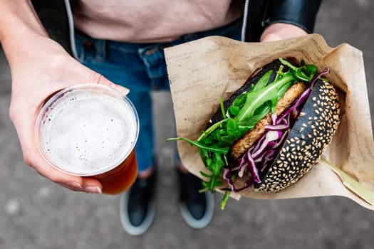 Close up of woman hands holding delicious organic salmon vegetarian burger and homebrewed IPA beer on open air beer an burger urban street food festival in Ljubljana, Slovenia