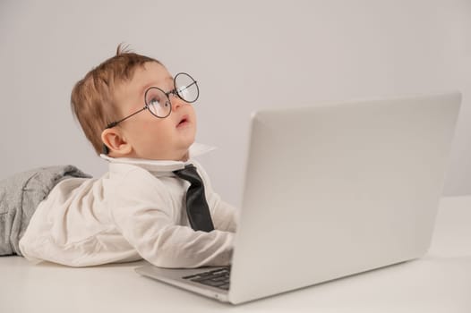 Cute baby in glasses and suit working on laptop