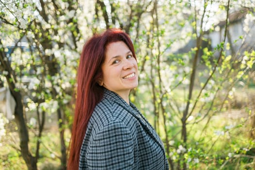 Beautiful red-haired woman enjoying smell in a flowering blooming spring garden. Spring blossom.