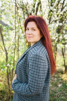 Beautiful red-haired woman enjoying smell in a flowering blooming spring garden. Spring blossom.