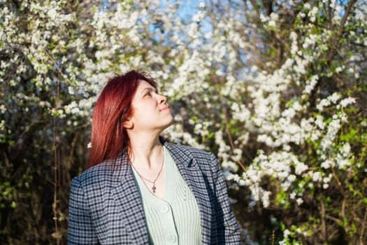 Beautiful red-haired woman enjoying smell in a flowering blooming spring garden. Spring blossom.