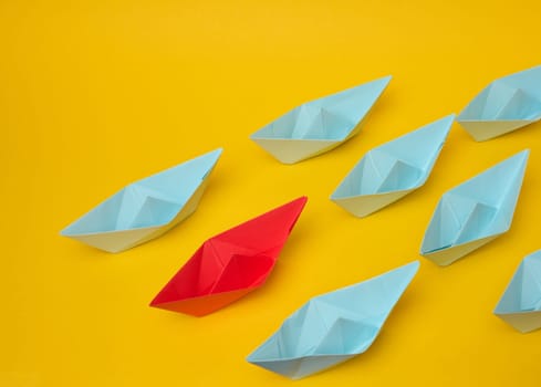 Group of blue paper boats follow red against a yellow background. Strong leader concept, mass manipulation. Starting a business with a well-coordinated team, start-up