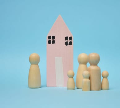 Wooden house and miniature figurines of a family on a blue background. The concept of selling and buying real estate, investment