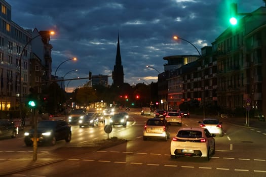 Hamburg, Germany - May 19, 2023: A city street at night filled with heavy traffic, cars, buses, and pedestrians moving hurriedly under the bright city lights.