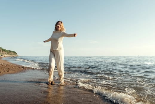 A woman stands on the sandy beach next to the vast ocean, gazing at the water under the clear blue sky on a sunny day.