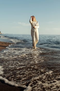 A woman is standing in the water at the beach, with waves gently lapping around her. She gazes out towards the horizon under the clear blue sky.