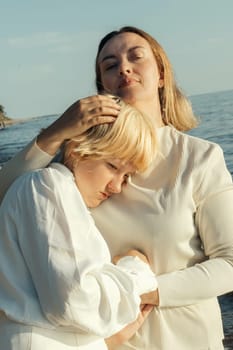 Mom hugs her daughter on the beach by the sea. Close-up.