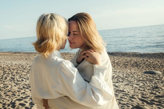 Mom and daughter are standing on the beach by the sea, hugging.