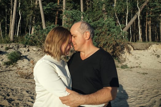 A man and woman are embracing each other on a sandy beach near the water under the clear blue sky.