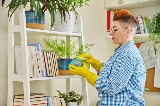 Middle-aged woman cleaning house, female wiping dust in room. Housekeeping, housework, housecleaning, cleaning concept