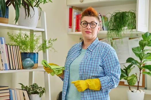 Middle-aged woman cleaning house, female looking at camera, wiping dust in room. Housekeeping, housework, housecleaning, cleaning concept