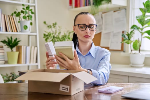 Dissatisfied indignant female customer buyer sitting at home unpacking cardboard box with online purchases. Surprised woman unpacking boxes with cosmetics care products perfumes. Delivery by mail online store