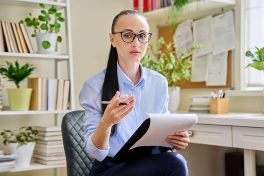 Portrait of confident female psychologist with clipboard at workplace in office. Professional mental therapist counselor psychologist social worker looking at camera. Health care service, treatment