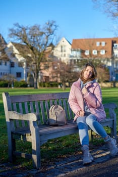 Embrace the tranquility of winter with this captivating image featuring a beautiful girl in a pink winter jacket, leisurely sitting on a bench in a park against the backdrop of a charming old European town. The photograph beautifully captures the serene atmosphere, blending the girl's winter style with the timeless charm of the historic surroundings. Winter Wonderland Elegance: Beautiful Girl in Pink Jacket Enjoys Festive Atmosphere in Bitigheim-Bissingen Park. Experience the magic of the holiday season as a charming girl in a pink winter jacket sits on a bench in a park against the backdrop of the historic town of Bitigheim-Bissingen, Baden-Württemberg, Germany. The scene is adorned with picturesque half-timbered houses, creating a delightful blend of winter charm and architectural beauty.